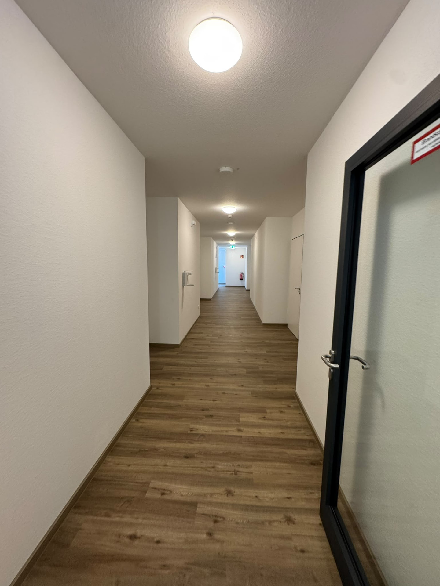 Langer Flur einer Wohnanlage mit Holzboden und weißen Wänden